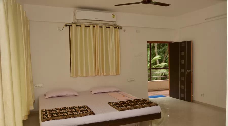 Room with double bed and door opening to a palm-view balcony